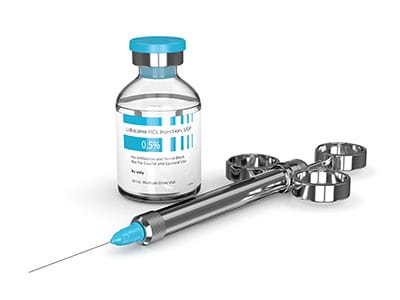 A needle next to a bottle. The bottle is labeled "lidocaine"